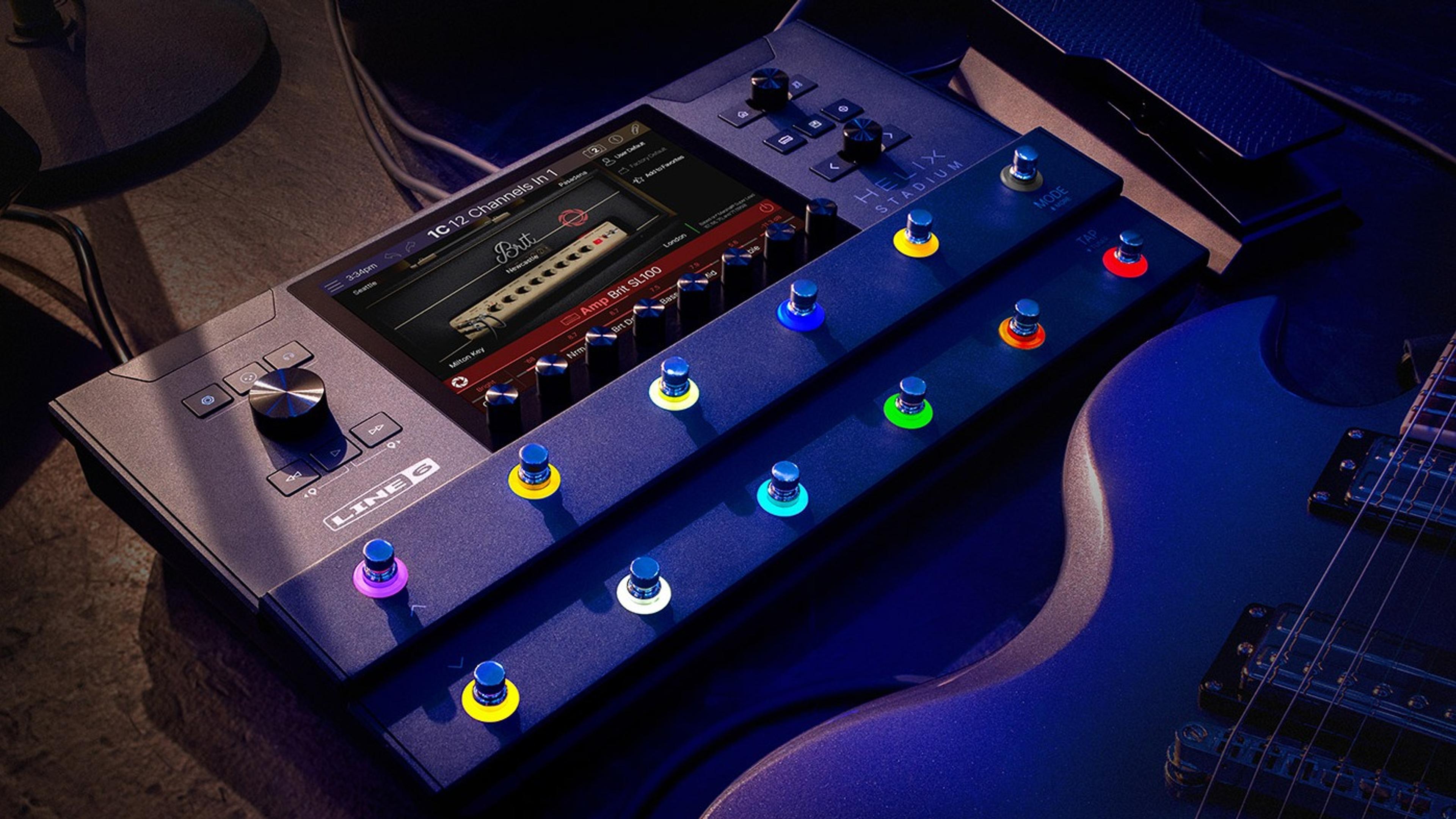 Line 6 Helix Stadium Floor on a dark stage floor beside an electric guitar, touchscreen showing the Brit SL100 amp block