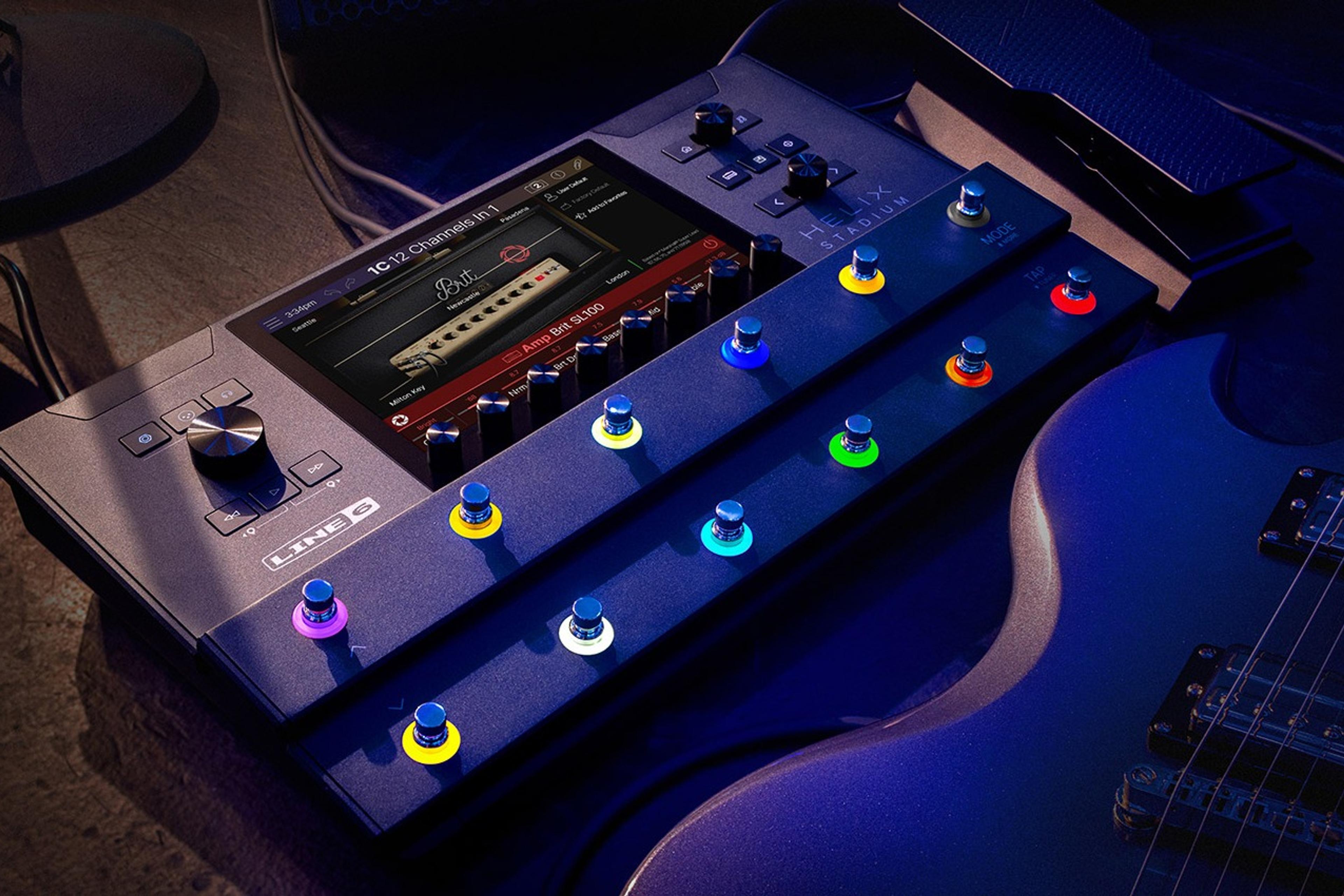 Line 6 Helix Stadium Floor on a dark stage floor beside an electric guitar, touchscreen showing the Brit SL100 amp block