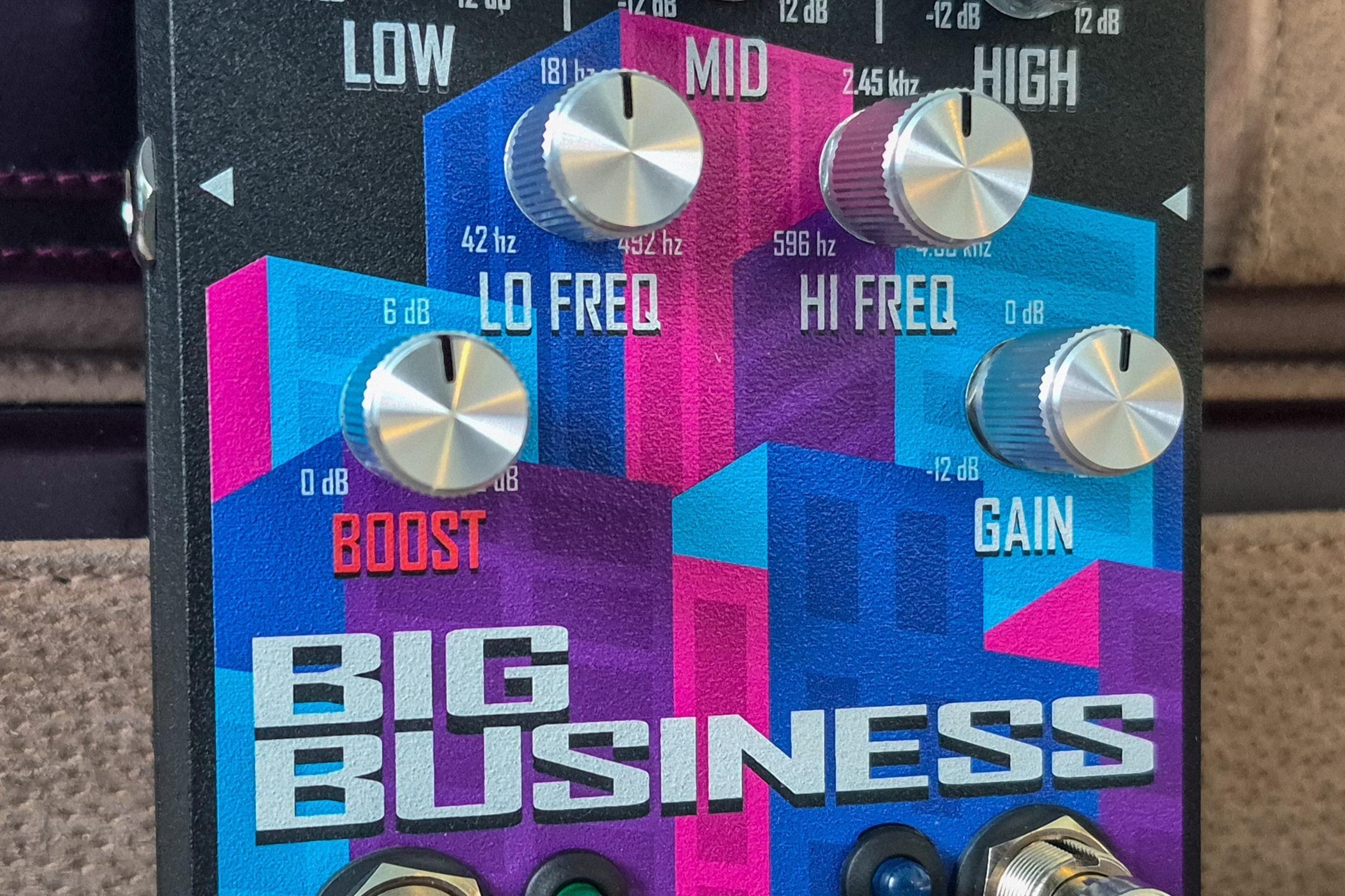 Turbulent Audio Big Business pedal standing on a beige leather surface in front of a brown leather briefcase, skyline graphic and eight silver knobs