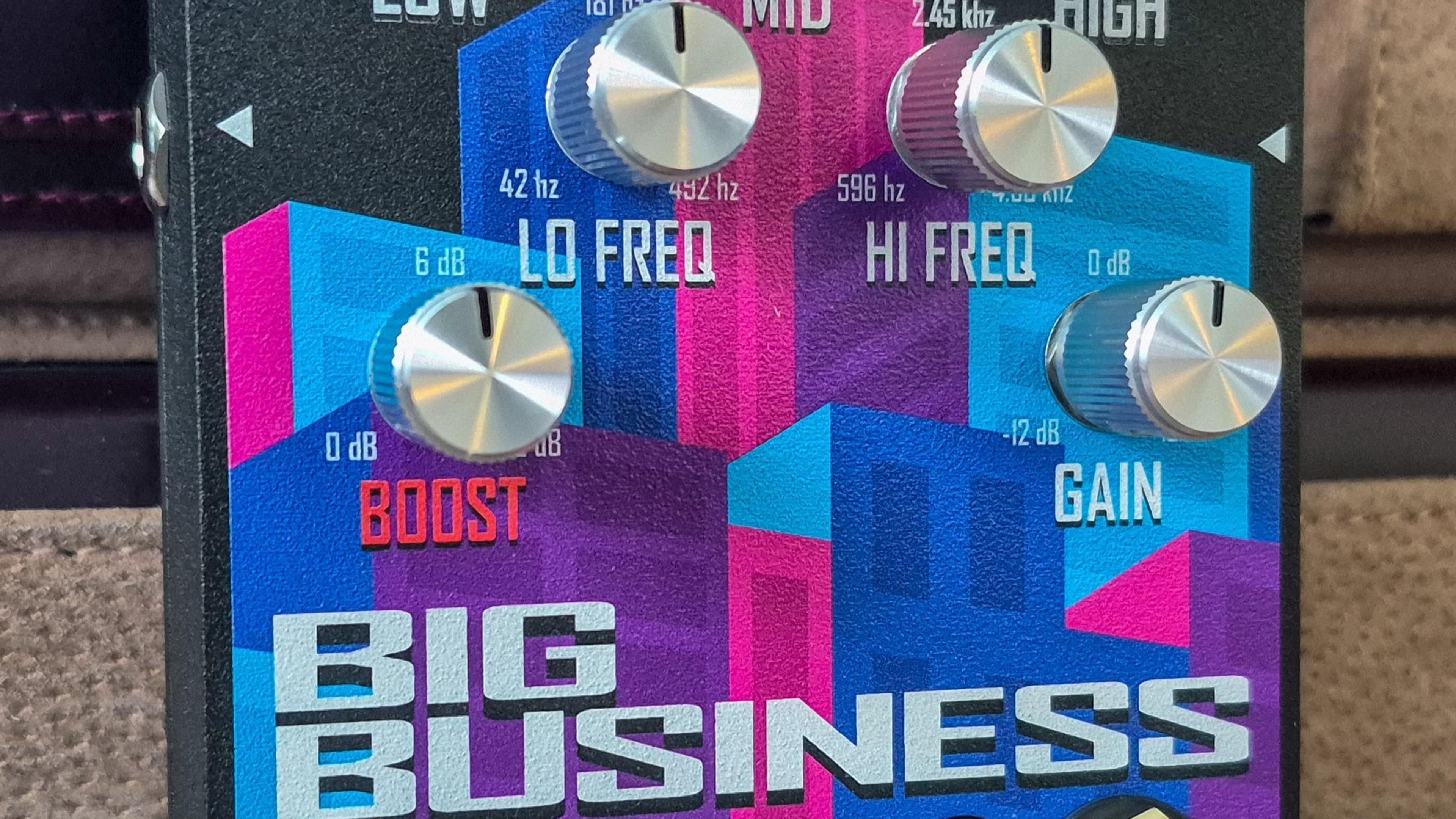 Turbulent Audio Big Business pedal standing on a beige leather surface in front of a brown leather briefcase, skyline graphic and eight silver knobs