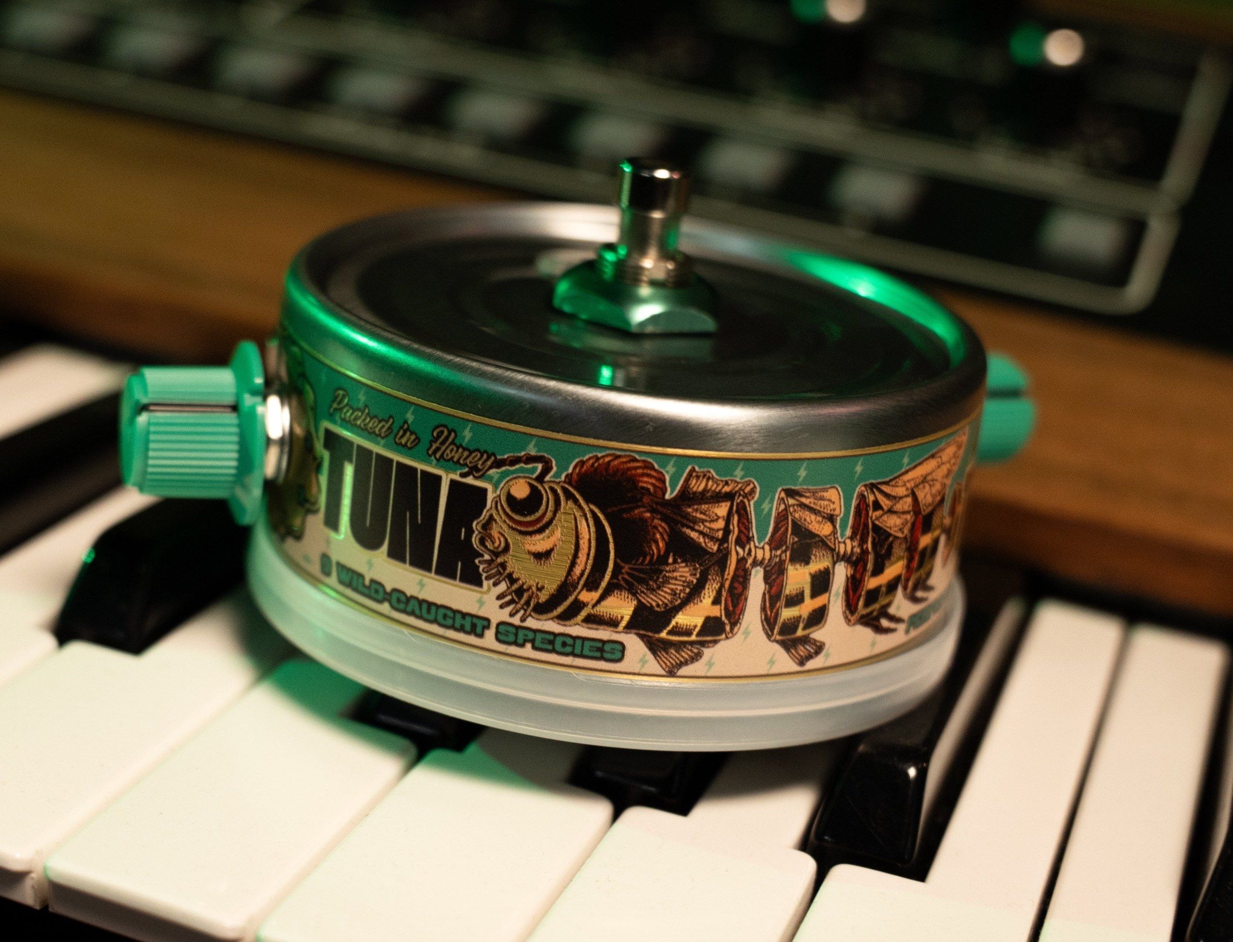 Beetronics Tuna Trem sitting on synth keys under green light, TUNA label with bee artwork and '9 wild-caught species' text