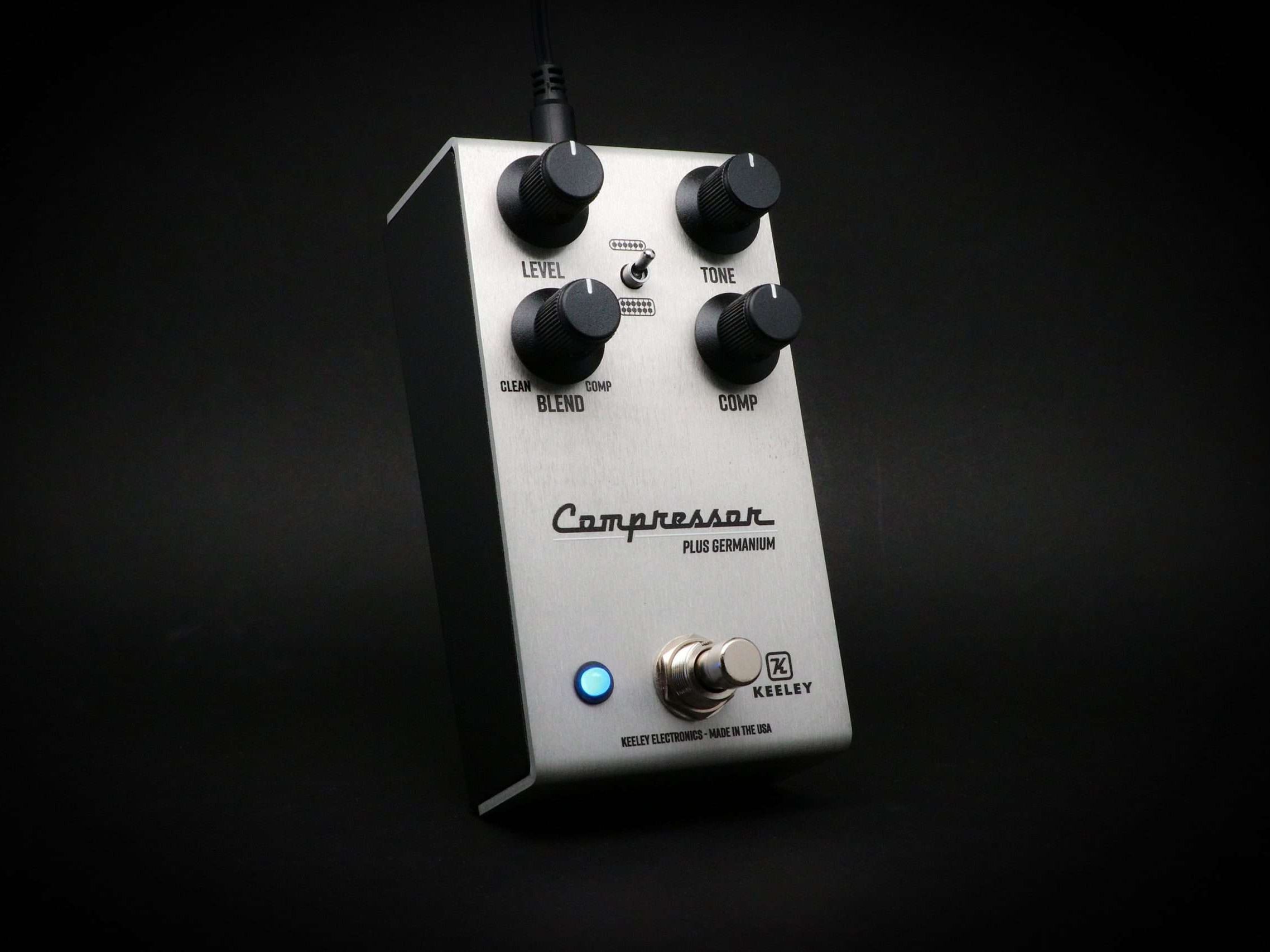 Keeley Compressor Plus Germanium in brushed aluminium, three-quarter view on a black backdrop with the blue status LED lit and Level, Tone, Blend and Comp knobs