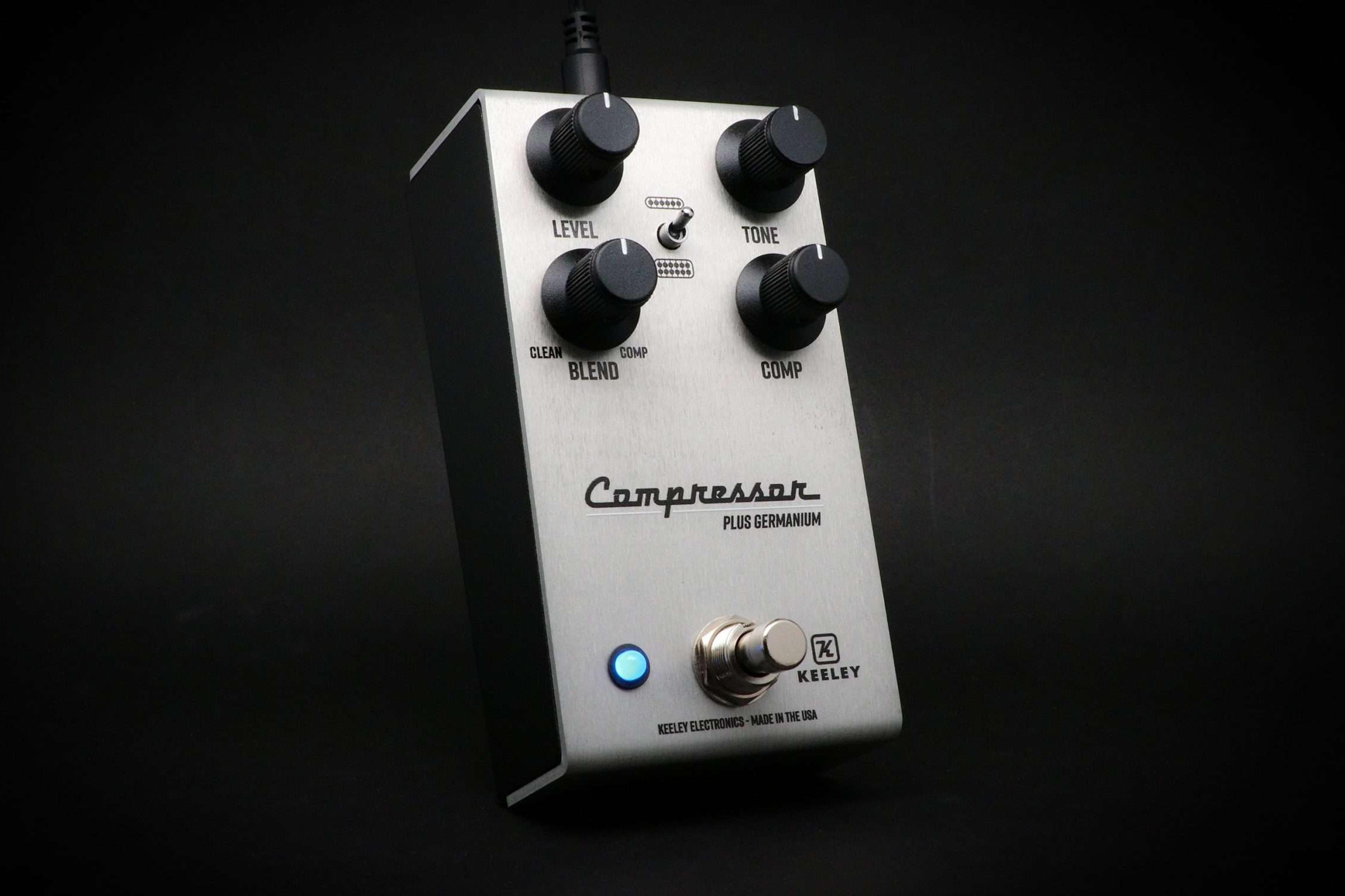 Keeley Compressor Plus Germanium in brushed aluminium, three-quarter view on a black backdrop with the blue status LED lit and Level, Tone, Blend and Comp knobs