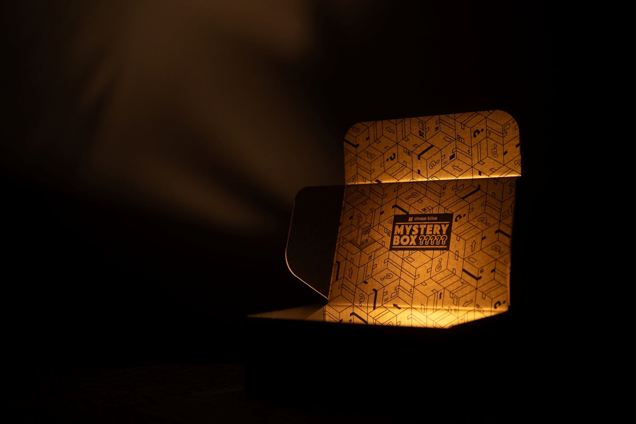 Open Chase Bliss Mystery Box glowing in the dark, its gold interior printed with question-mark boxes and a Mystery Box label