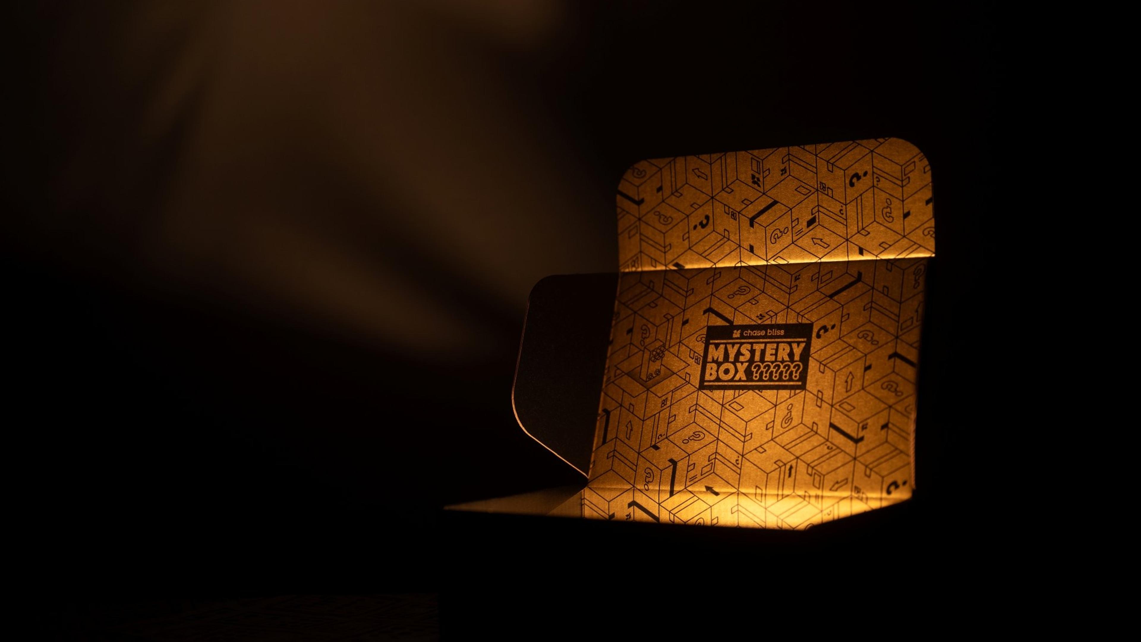 Open Chase Bliss Mystery Box glowing in the dark, its gold interior printed with question-mark boxes and a Mystery Box label