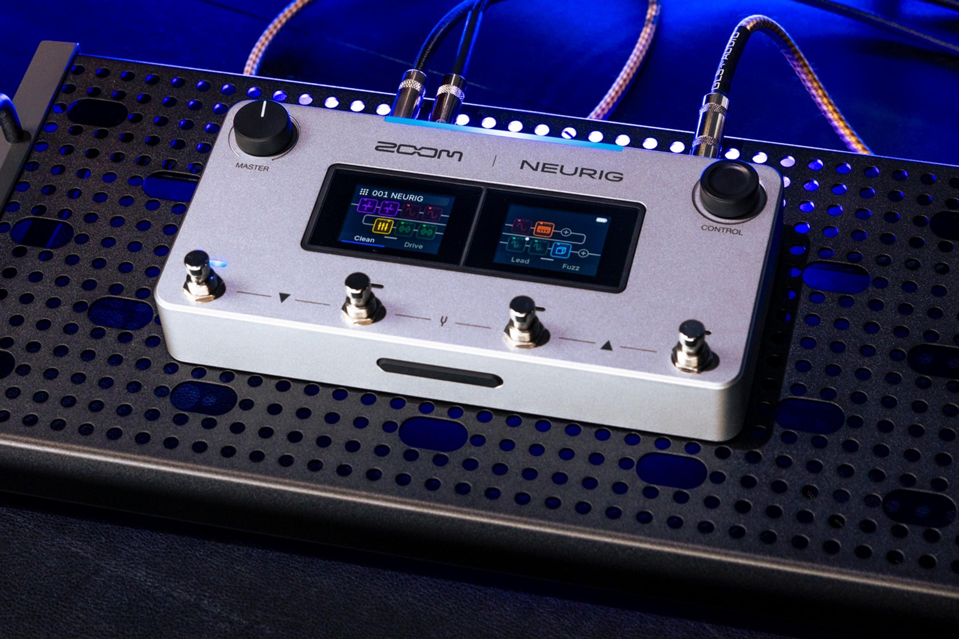ZOOM NEURIG on a black perforated pedalboard under blue stage light, dual touchscreens lit and cables in the top jacks