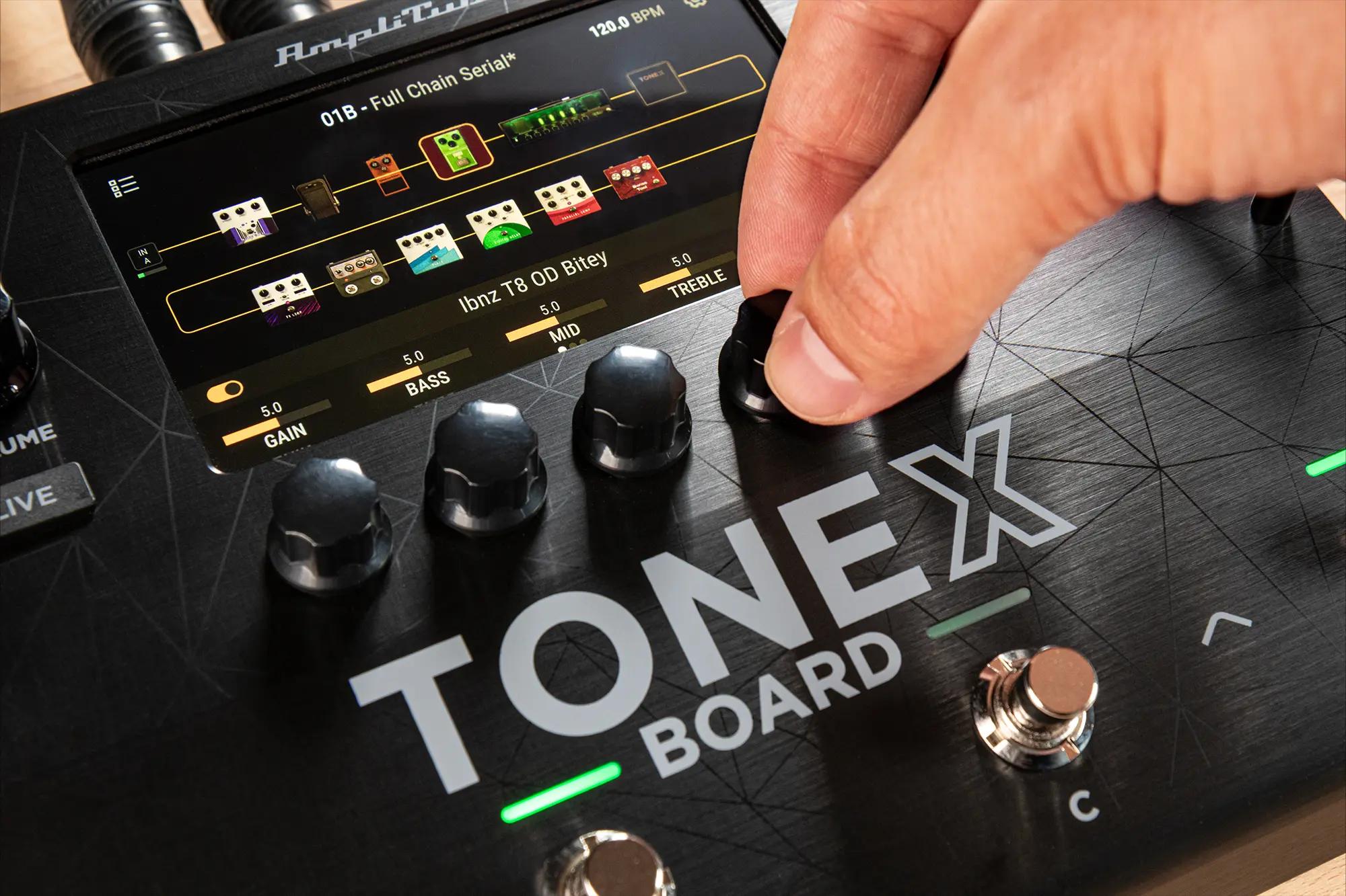 Hand adjusting knobs on an IK Multimedia TONEX Board, colour display showing a full amp and effects chain