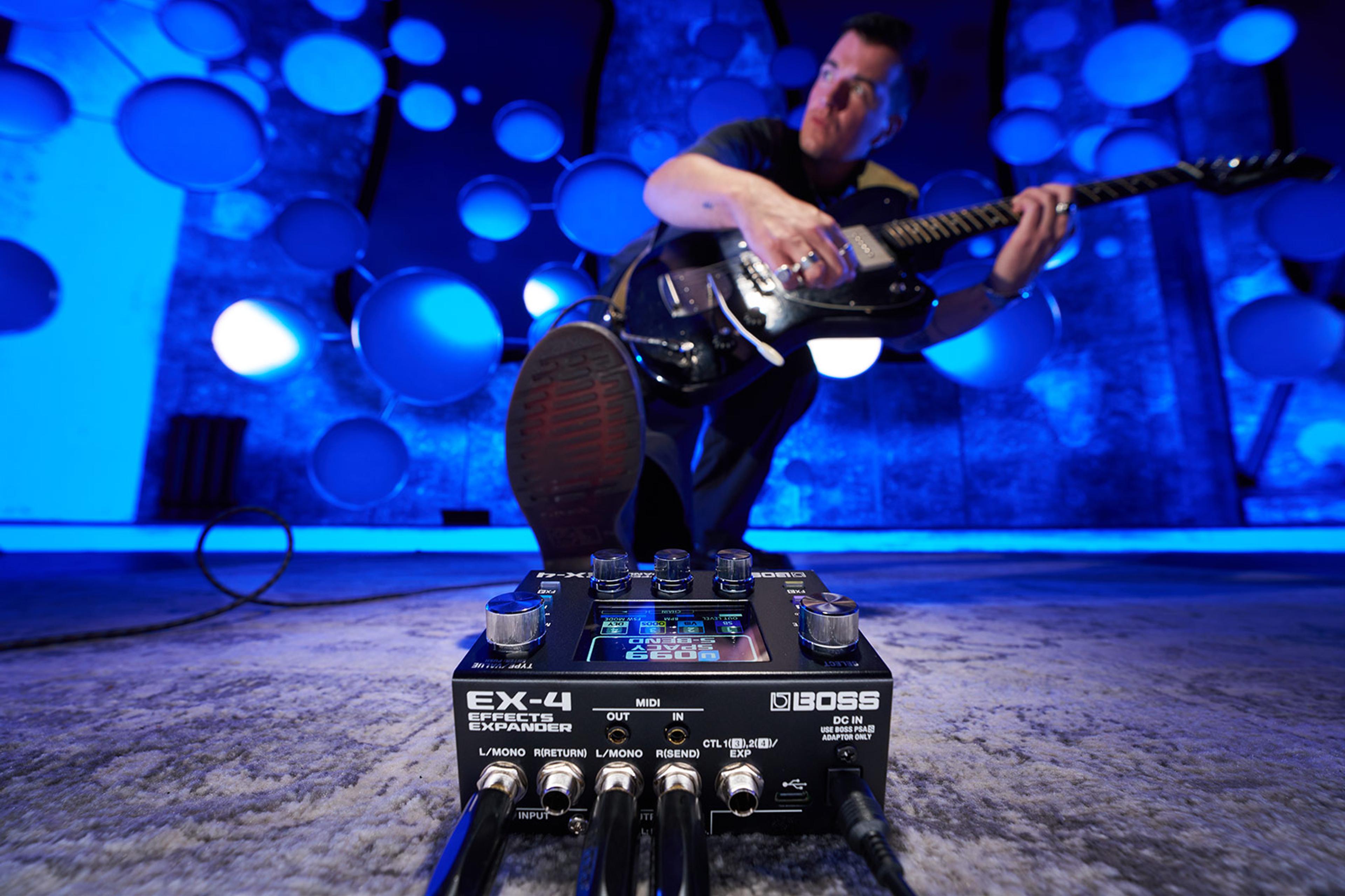 Boss EX-4 Effects Expander on a studio floor with a guitarist playing in a blue-lit room behind it