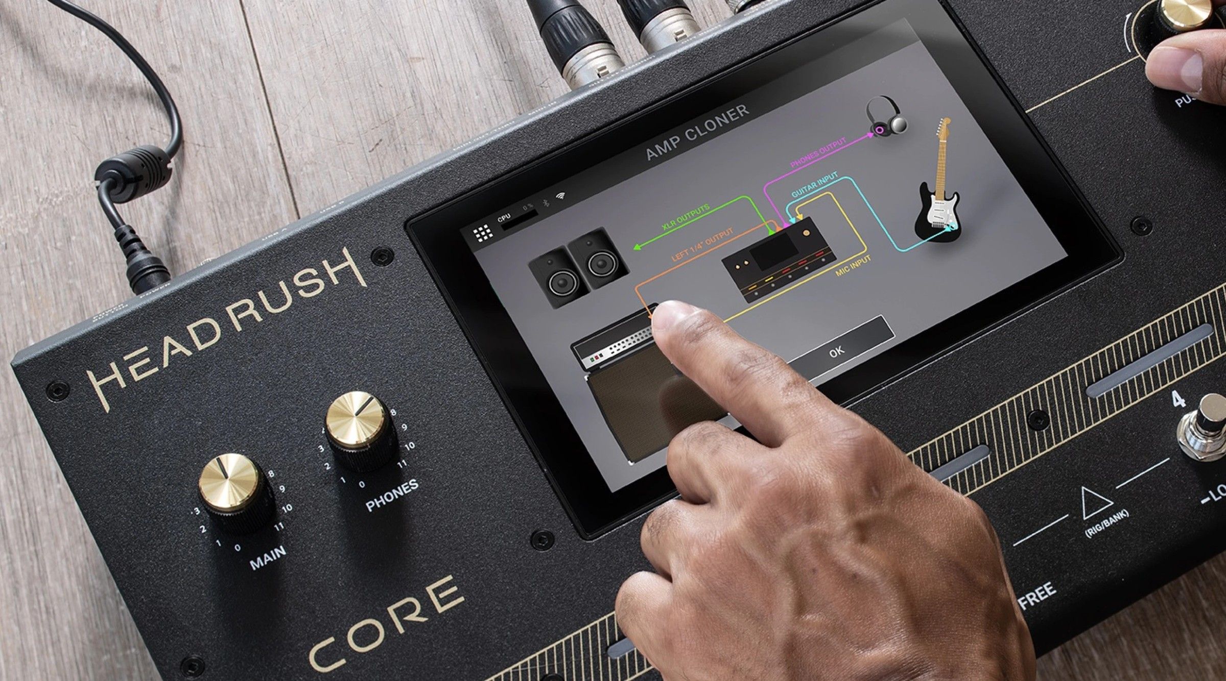 A finger tapping the HeadRush Core touchscreen, which shows the Amp Cloner screen