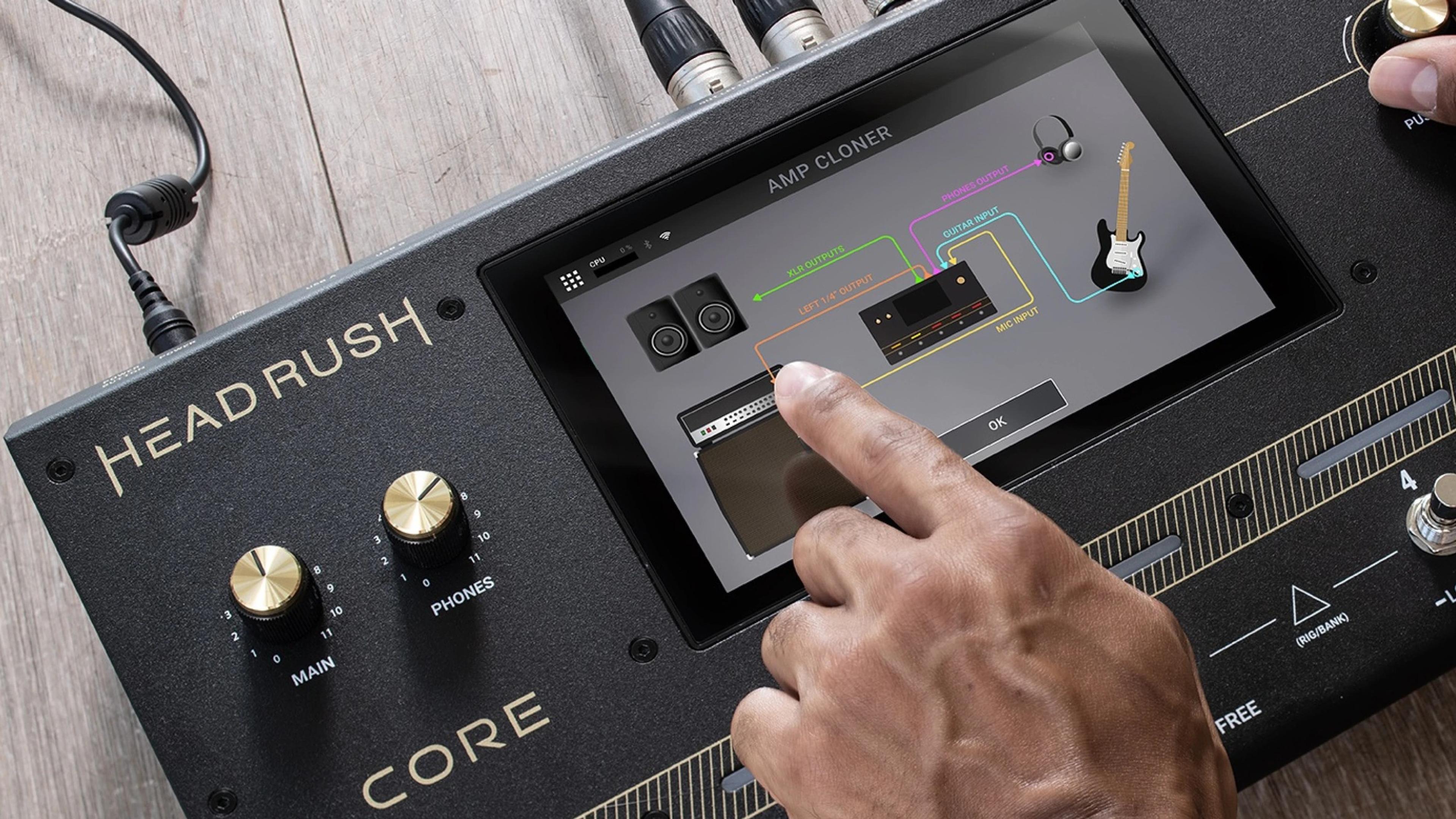 A finger tapping the HeadRush Core touchscreen, which shows the Amp Cloner screen