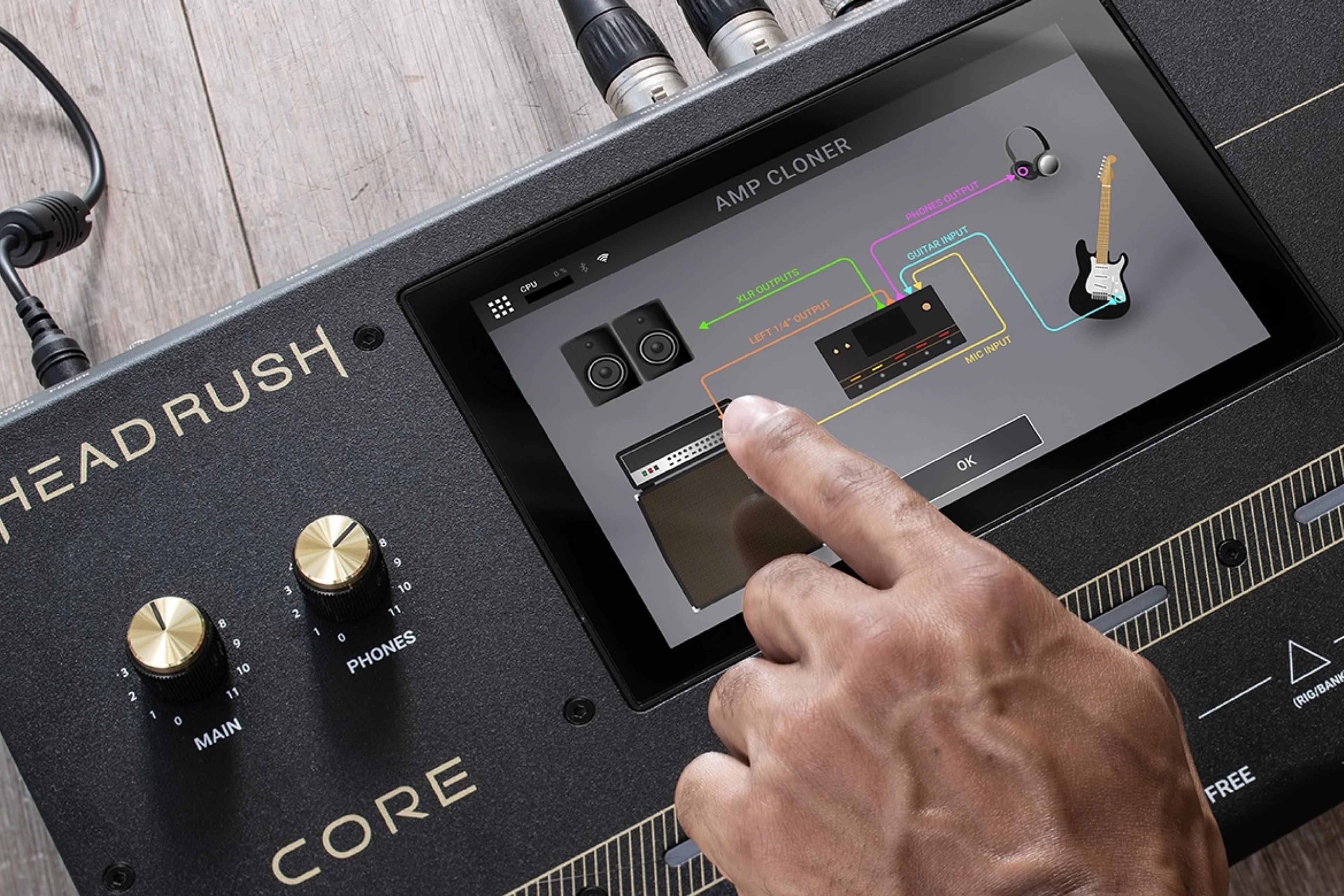 A finger tapping the HeadRush Core touchscreen, which shows the Amp Cloner screen
