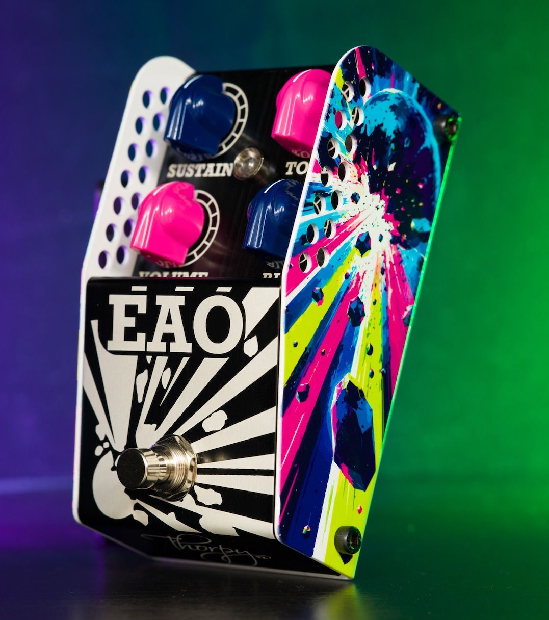 ThorpyFX EAO fuzz at an angle on a purple and green lit backdrop, showing pink and blue knobs and the explosion artwork on its side panel