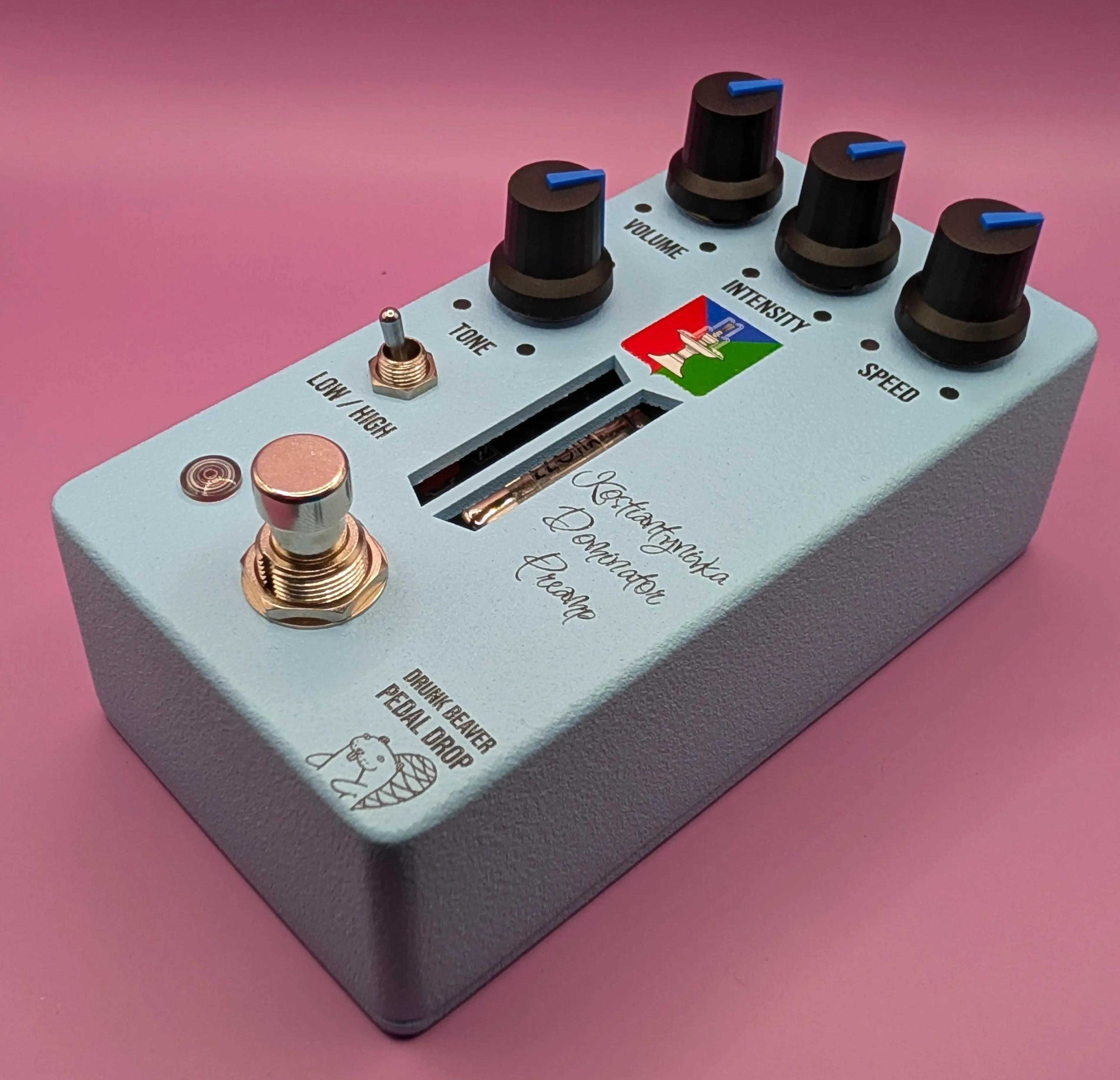 Drunk Beaver Kostiantynivka Dominator Preamp, three-quarter view on a pink backdrop, pale blue enclosure with Tone, Volume, Intensity and Speed knobs