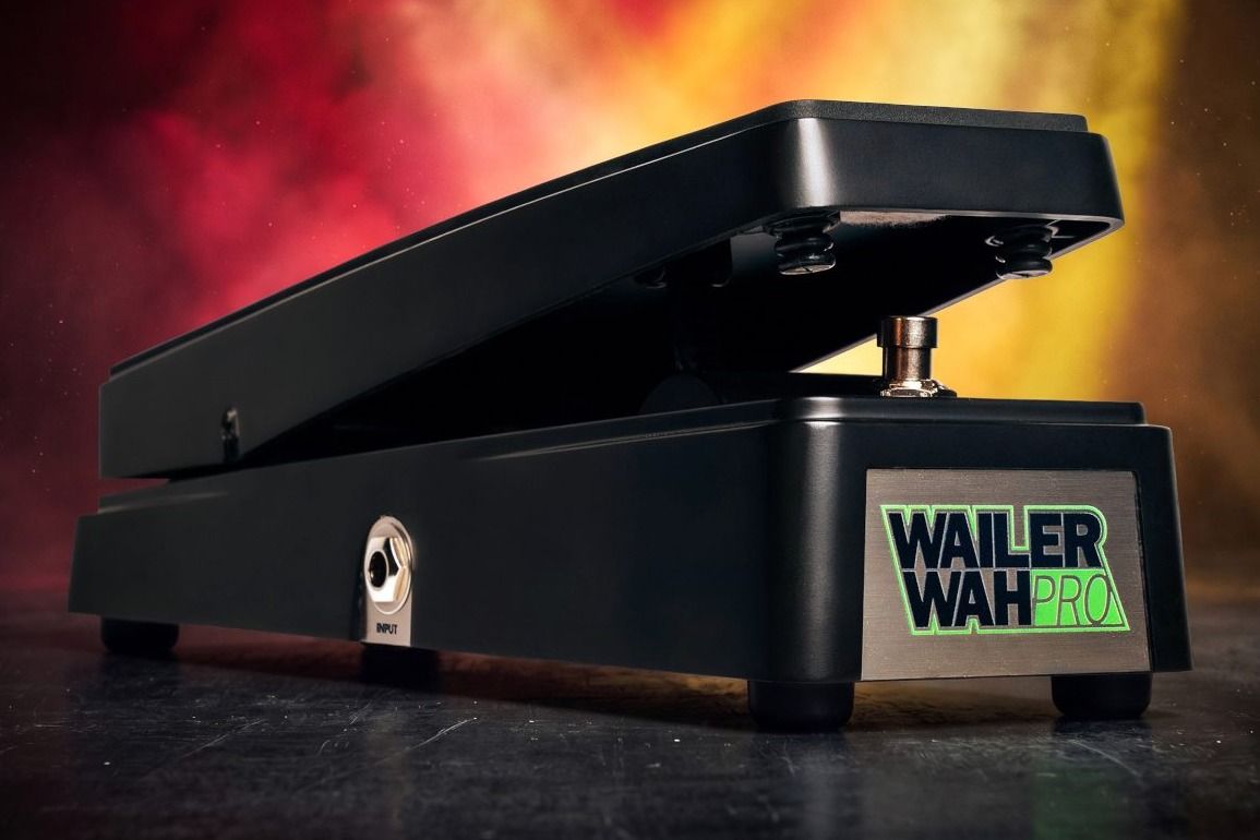 Electro-Harmonix Wailer Wah Pro on a dark stage floor in front of red and amber smoke, black die-cast treadle with the green Wailer Wah Pro nameplate