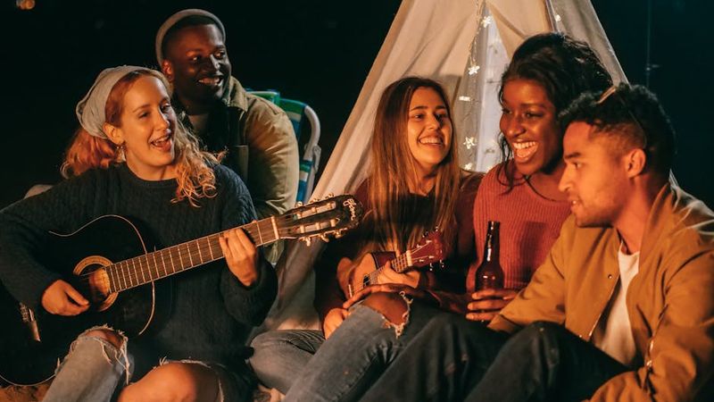 A group of friends enjoying a musical evening with guitars by a campfire at night.