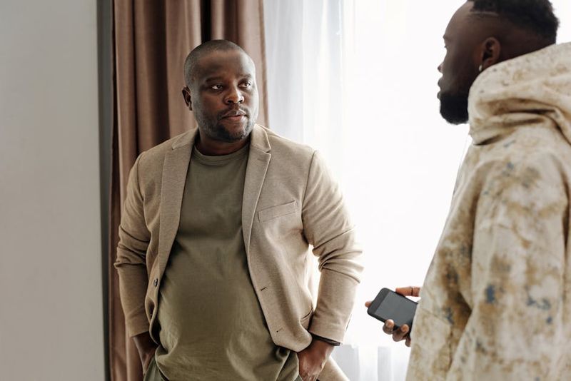 Two men engaged in a serious conversation indoors, one holding a smartphone.