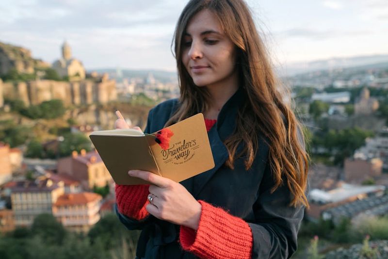 Eine Frau schreibt in ihr Tagebuch vor der Kulisse einer historischen Stadtlandschaft.