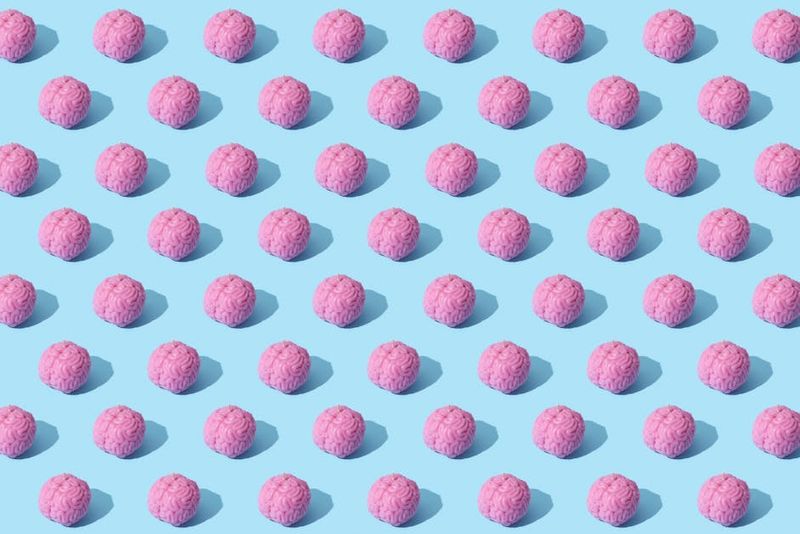 Creative composition of pink brain models in a repeating pattern on a light blue surface, showcasing abstract thinking.
