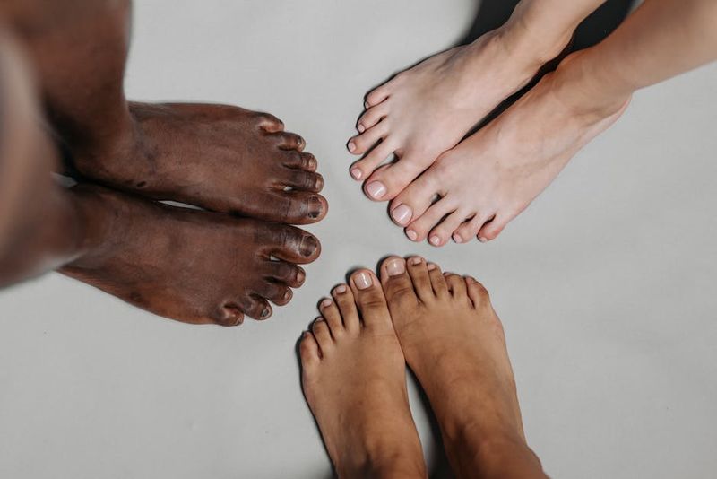 Close-up of diverse feet standing together on a neutral surface, symbolizing unity.