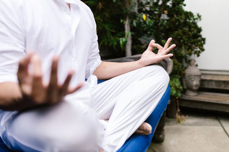 Una persona in bianco che pratica yoga e meditazione all'aperto in un ambiente sereno.