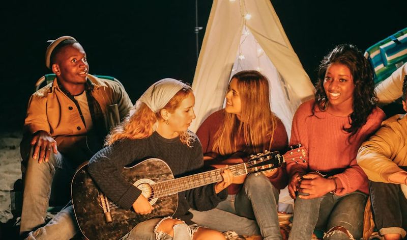Um grupo de amigos curtindo música e união em uma fogueira na praia à noite.