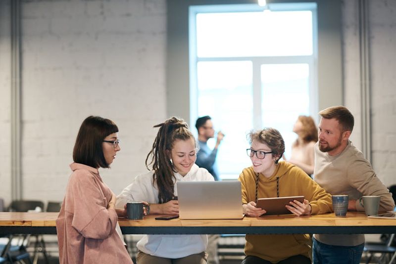 A group of young professionals collaborating indoors with laptops and tablets.