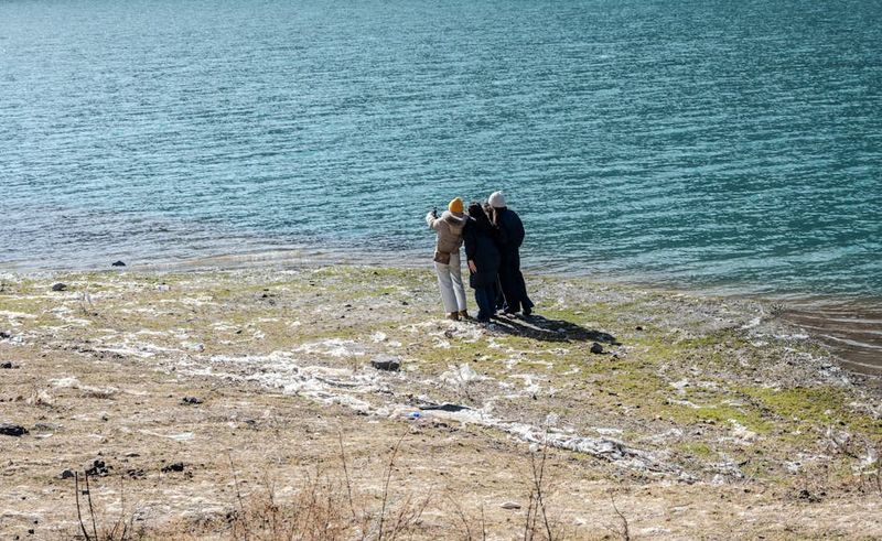 Trois personnes prenant un selfie au bord d'un lac, profitant d'une journée ensoleillée en plein air.