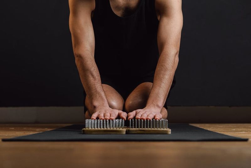 Adult man kneeling on a yoga mat practicing mindfulness with a sadhu board.