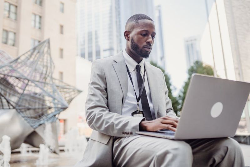 Profesional de negocios usando una laptop en un entorno urbano al aire libre. Enfocado en tareas de trabajo remoto.