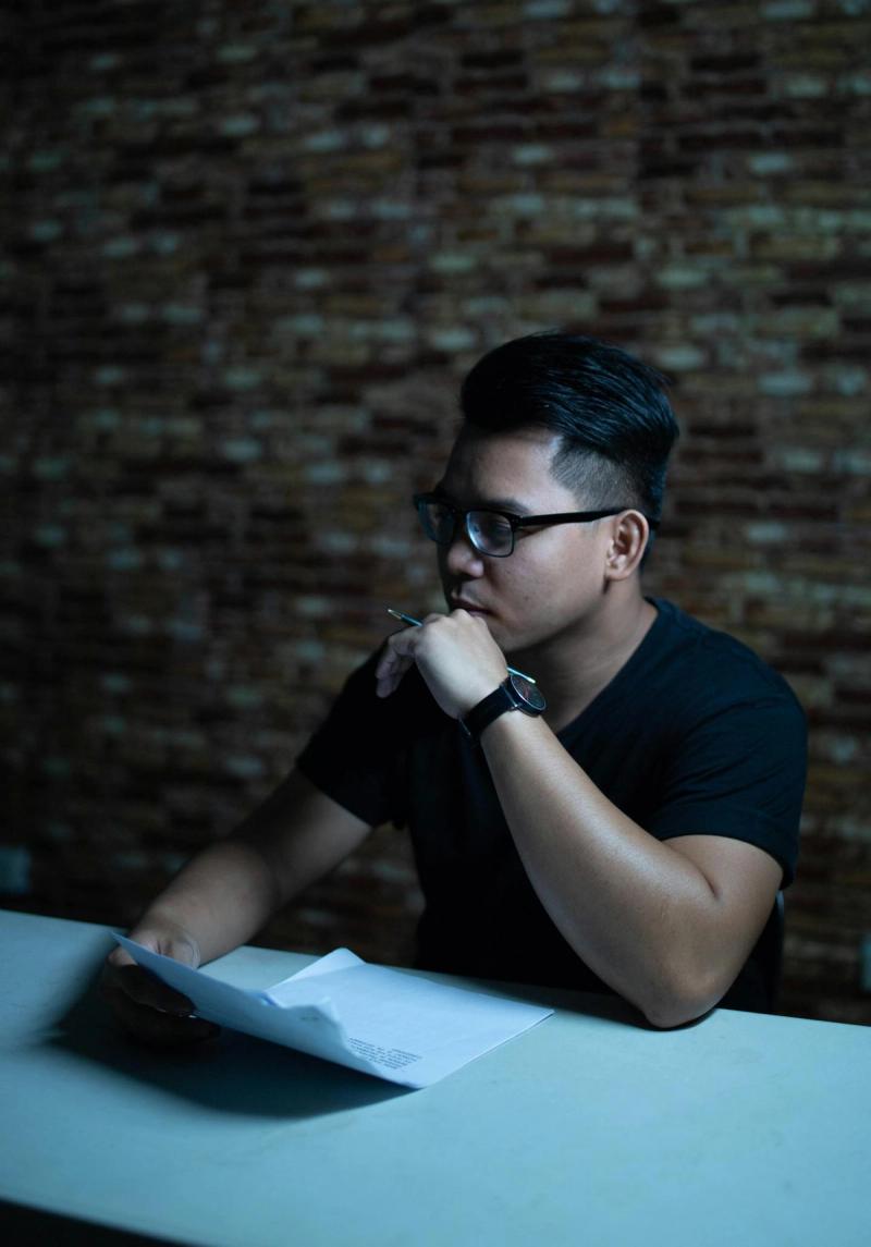 Man wearing glasses thinking with a pen at a table indoors