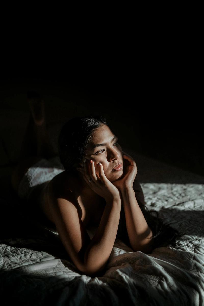 劇的な陽光の中、ベッドに横たわり内省する物思いにふける女性。