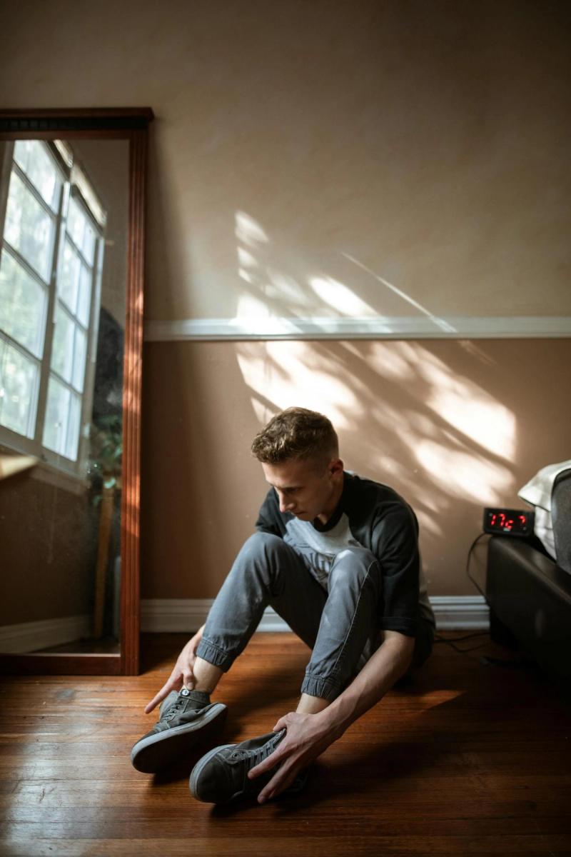 A young man sitting on the floor near a window, lost in thought.
