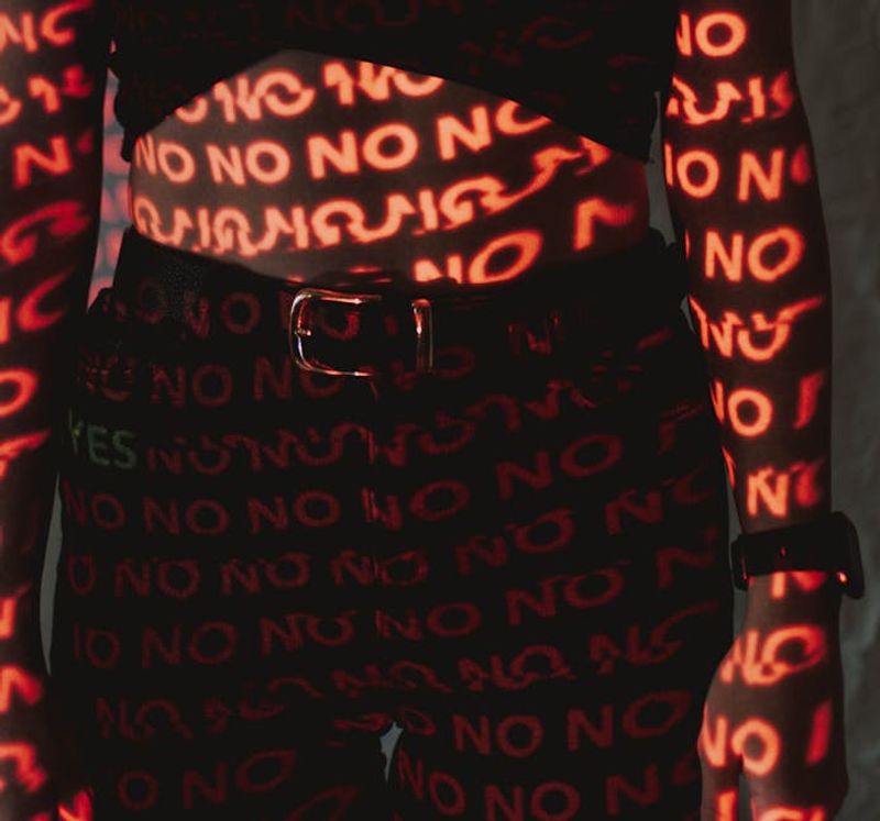 Illuminated words projected on a body creating a conceptual design with 'NO' text in red light.