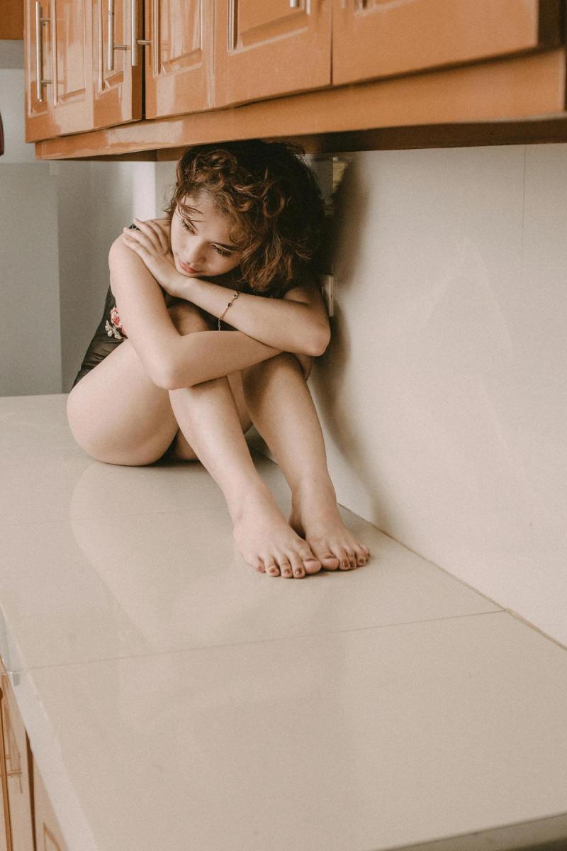 Young woman sits reflectively on a clean marble countertop indoors, capturing a moment of solitude.