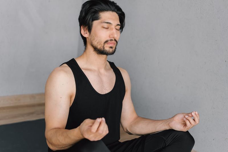 Un giovane uomo con la barba medita al chiuso, con gli occhi chiusi, in una posa del loto tranquilla.