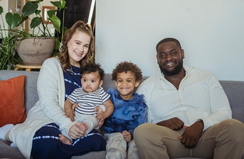 Uma família multirracial alegre de quatro pessoas sentada em um sofá, mostrando união e amor.