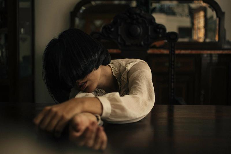 A woman in deep thought rests her head on a polished wooden table.