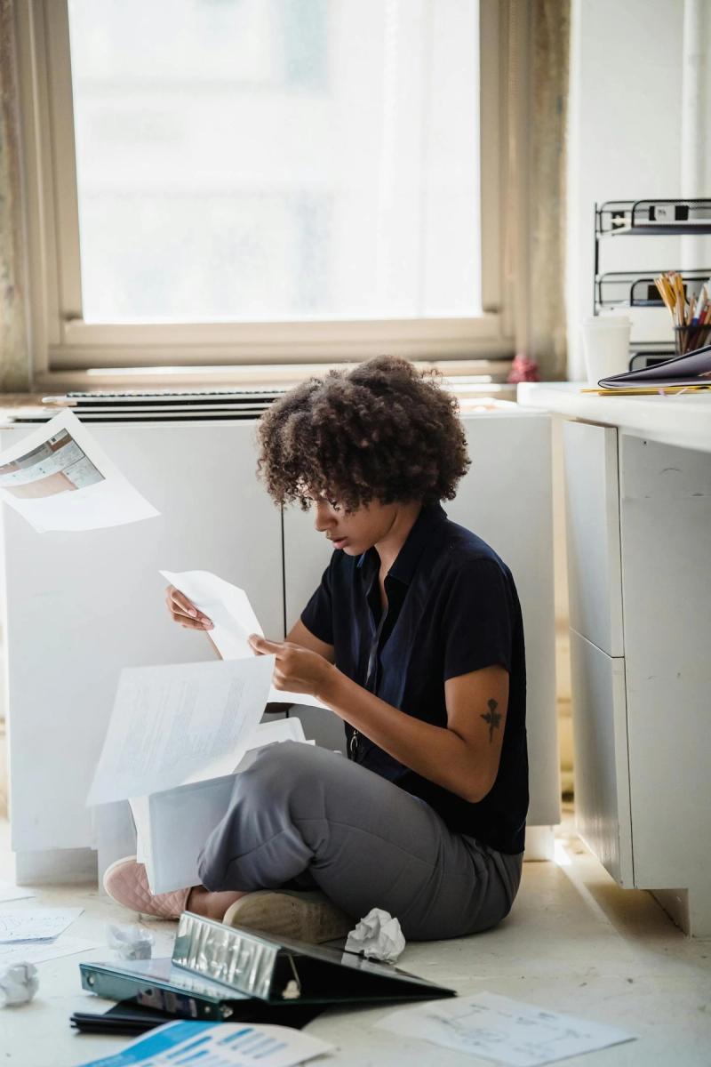 Young professional woman sorting paperwork on the floor in a modern office setting.