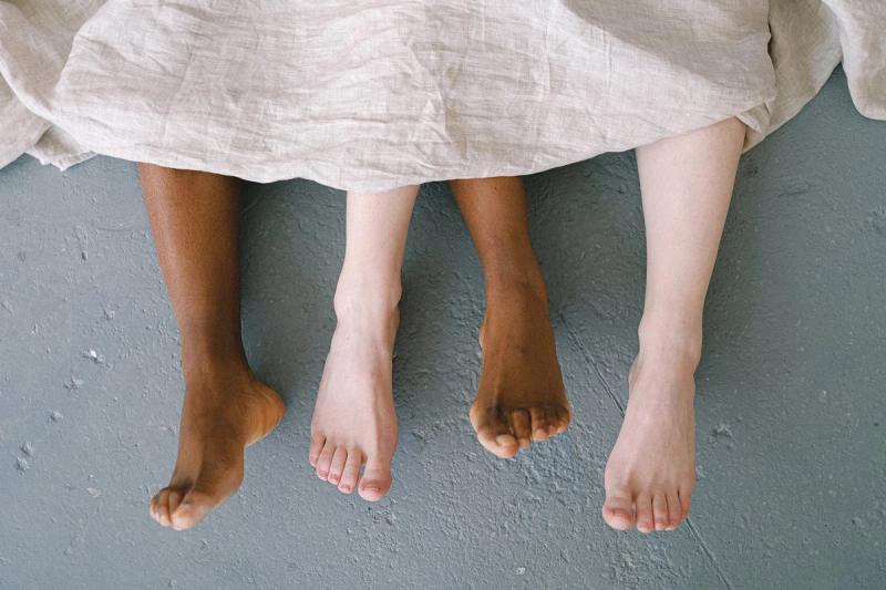 Füße eines interrassischen Paares liegen auf dem Boden und symbolisieren Liebe und Vielfalt.