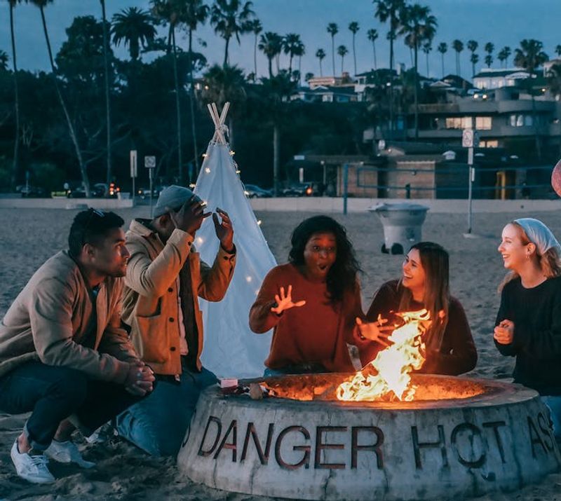 A diverse group of friends enjoying a bonfire on the beach at sunset, highlighting fun and togetherness.