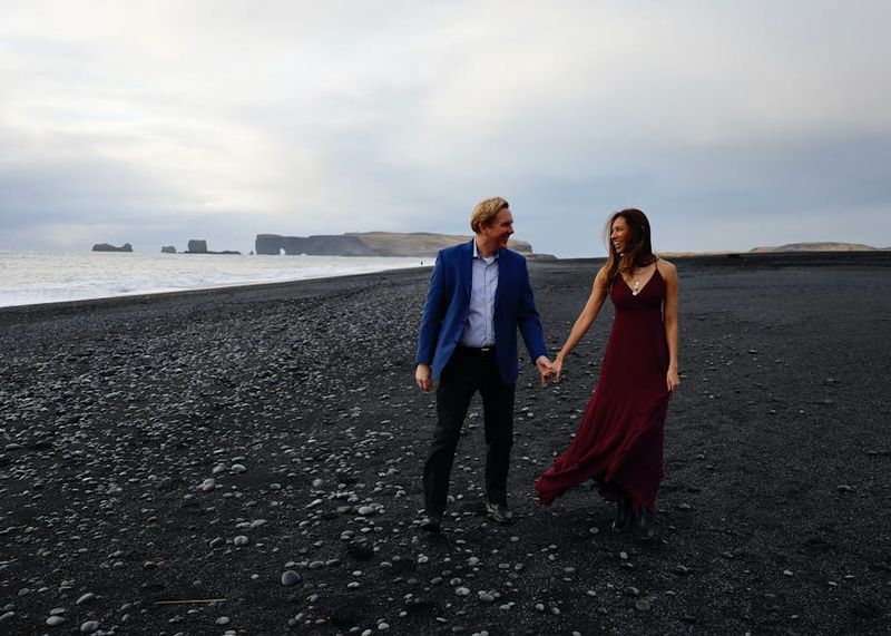Couple walking hand in hand on the black sand beach of Vík í Mýrdal, creating a romantic moment.