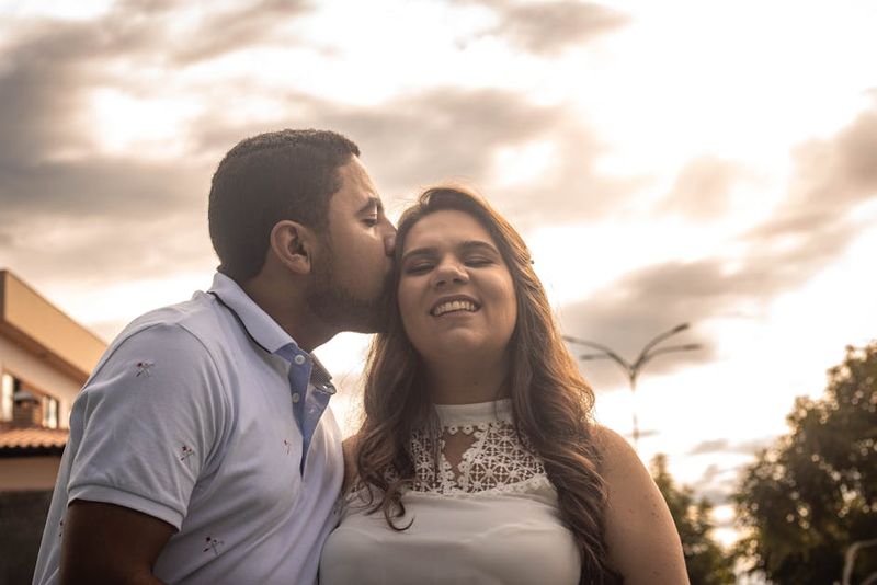 A joyful couple sharing an affectionate moment outdoors with a scenic cloudy sky.