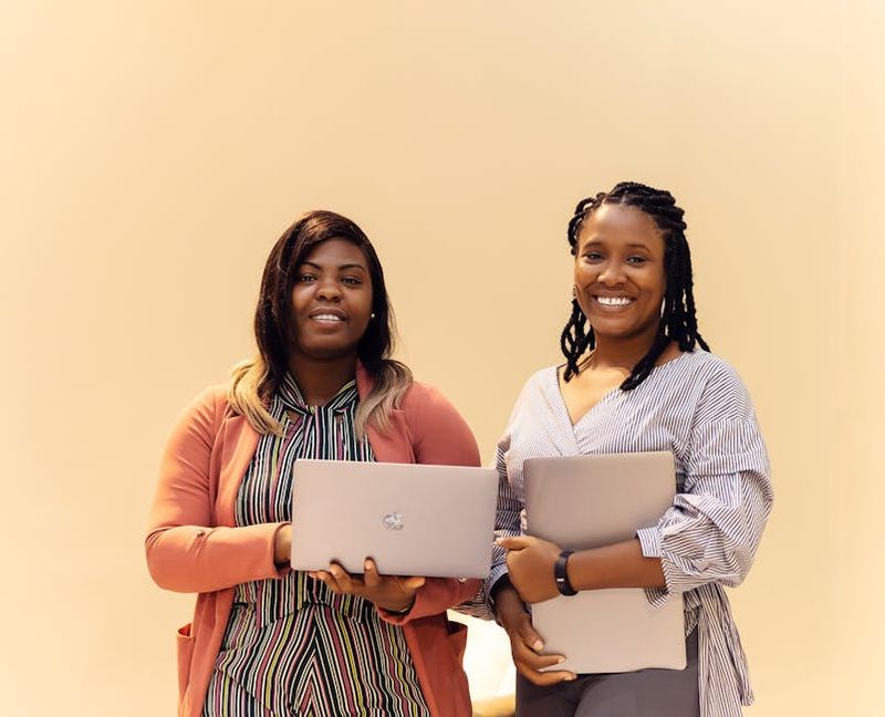 Professional African businesswomen smiling while working with laptops in a modern Lagos office setting.