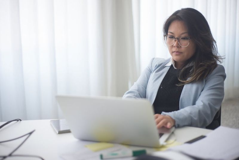 Focused businesswoman in office working on laptop with documents on the desk.