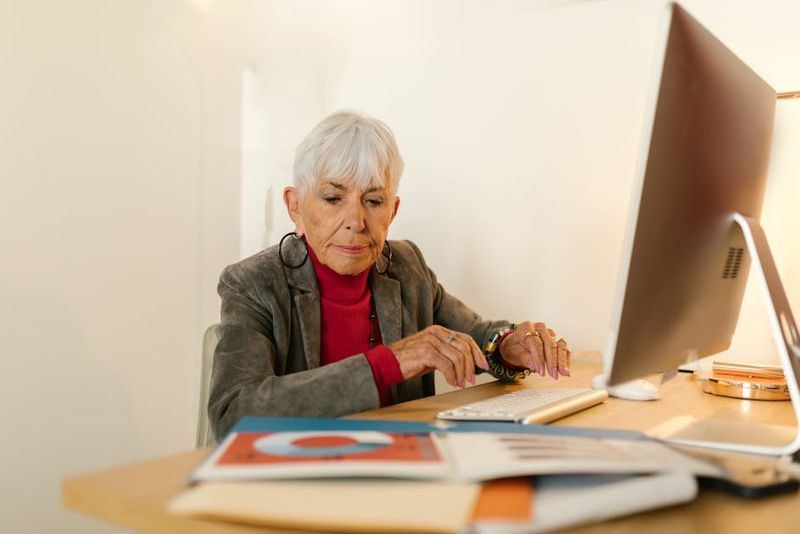 Senior woman in business attire focusing on her work at a modern office desk.