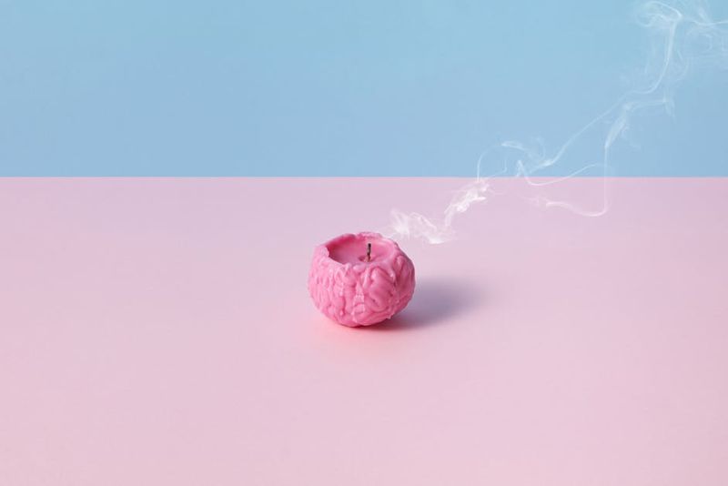 Imagem conceitual de uma vela rosa em forma de cérebro com fumaça, em um fundo rosa pastel e azul, simbolizando o esgotamento.