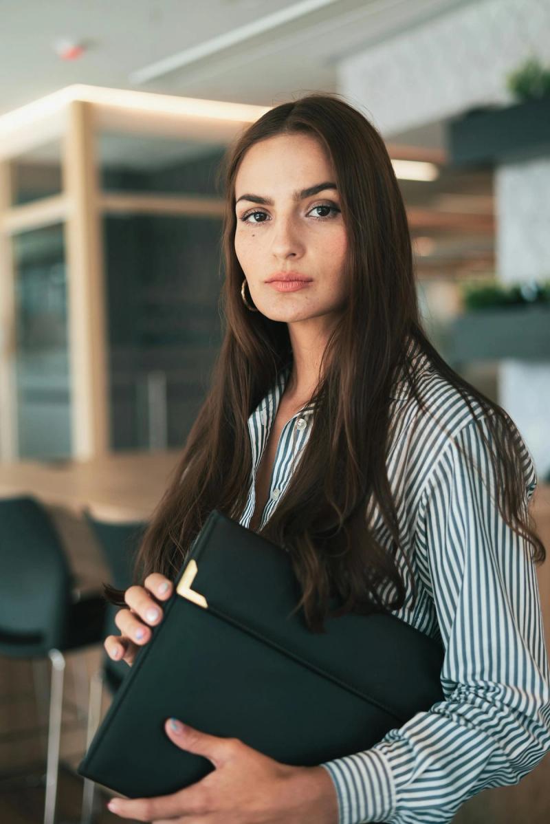 Retrato de uma empresária confiante com cabelo comprido segurando documentos em um escritório moderno.