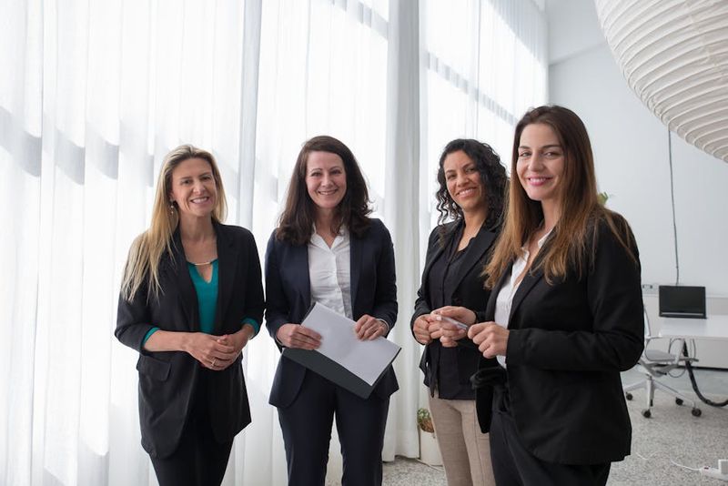 Four professional women in business attire smiling in a bright, modern office.