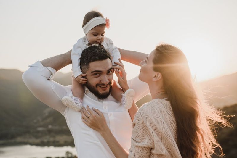 A joyful family moment with parents holding their baby outdoors at sunset.