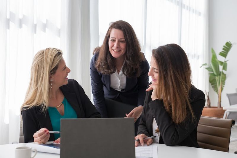 Tres mujeres profesionales involucradas en una discusión de negocios colaborativa en un entorno de oficina moderno.